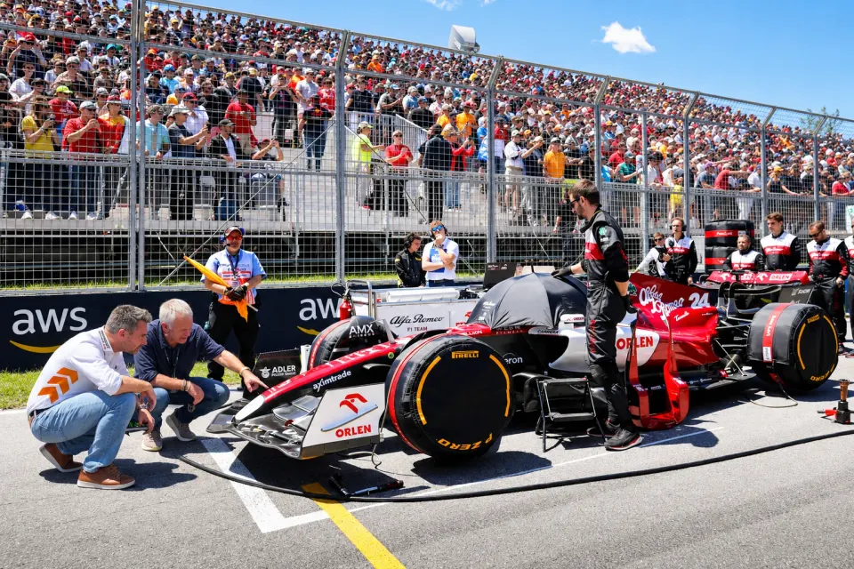 Formel-1-Rennwagen und Team in der Startaufstellung vor einer gefüllten Tribüne